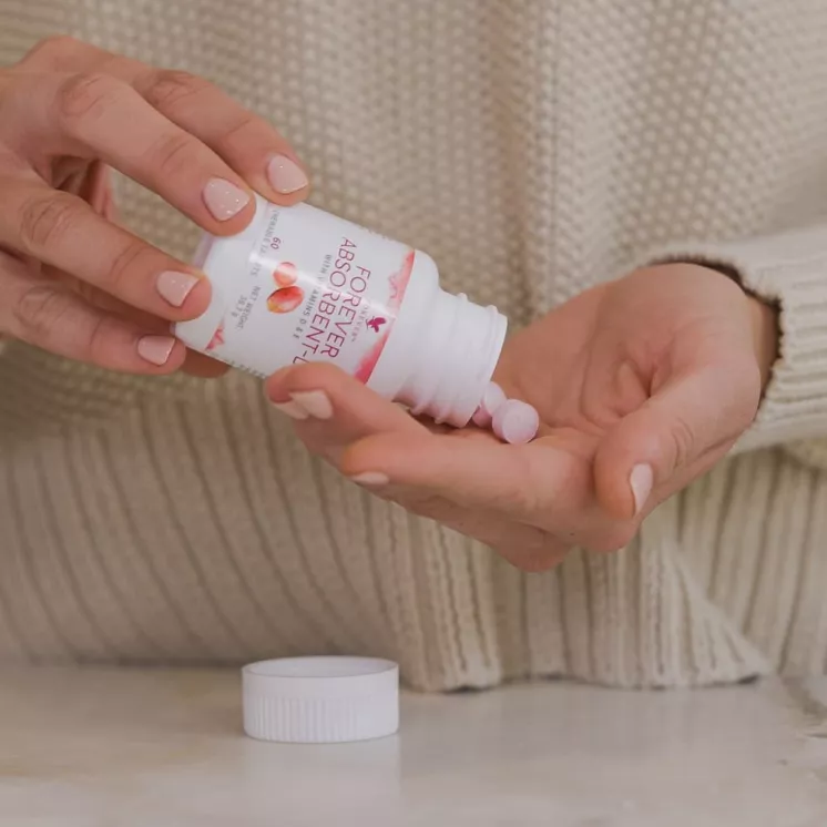 Personne tenant un flacon de Forever Absorbent-D et distribuant des comprimés de vitamines à mâcher dans la main.
