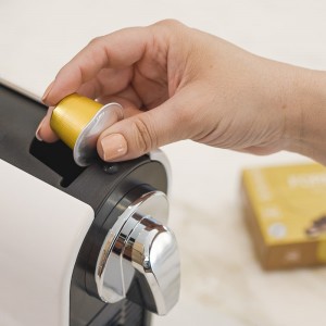 Main insérant une capsule dorée de Forever MÓR dans une machine à café Nespresso®, illustrant la facilité de préparation