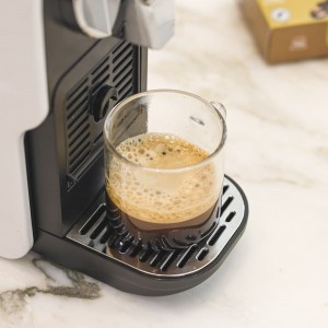 Café Forever MÓR prêt à être dégusté, préparé dans une machine Nespresso® à côté de la boîte de capsules enrichies en vitamines