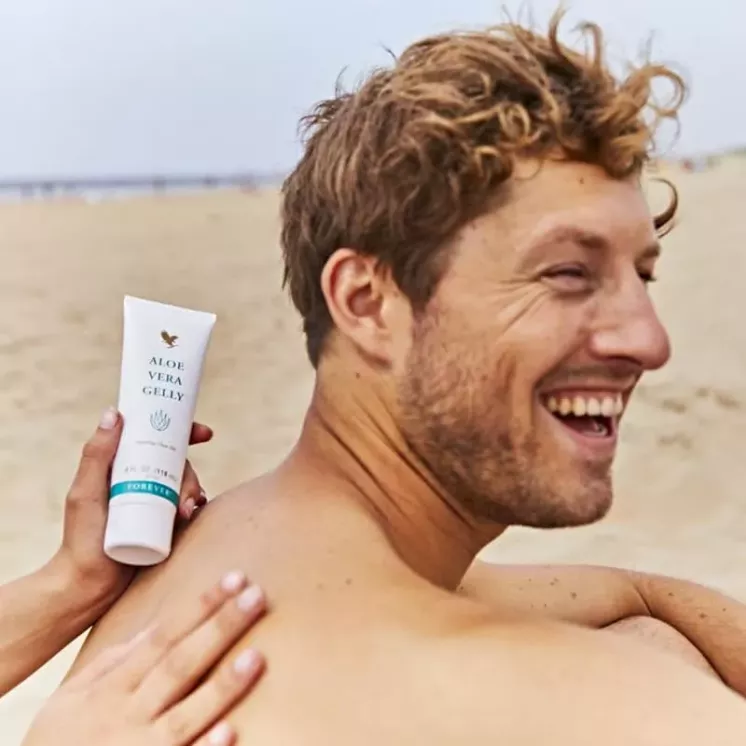 Application de Forever Aloe Vera Gelly sur le dos d’un homme à la plage, soulageant la peau sous le soleil.