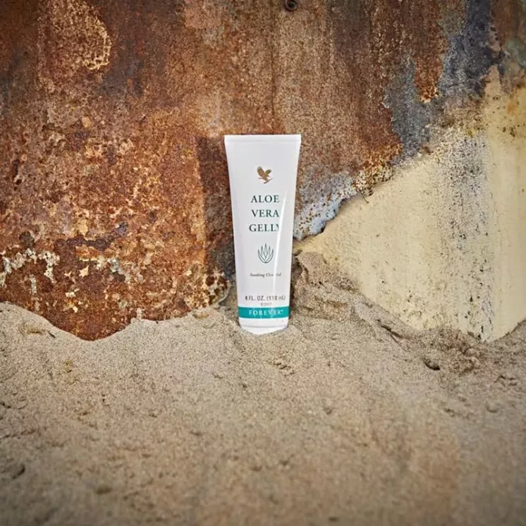 Tube de Forever Aloe Vera Gelly posé dans le sable, idéal pour apaiser la peau après une journée en plein air.