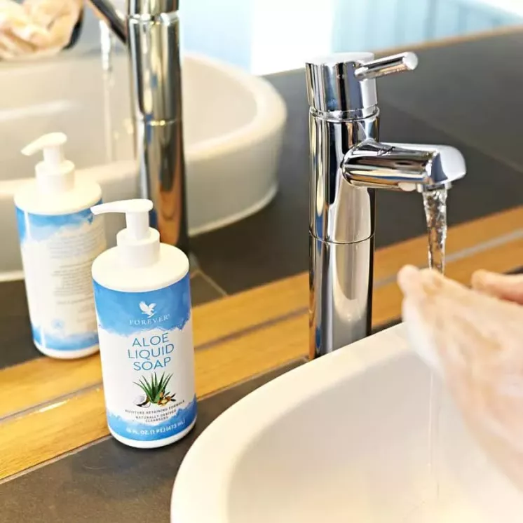 Bouteille de Forever Aloe Liquid Soap posée près d’un lavabo, reflétée dans le miroir d’une salle de bain élégante.