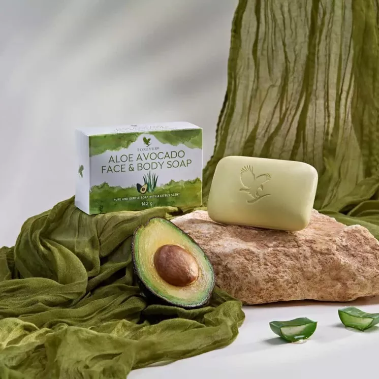 Savon Aloe Avocado Face & Body Soap de Forever Living sur un fond naturel avec un avocat coupé et des morceaux d’Aloe Vera