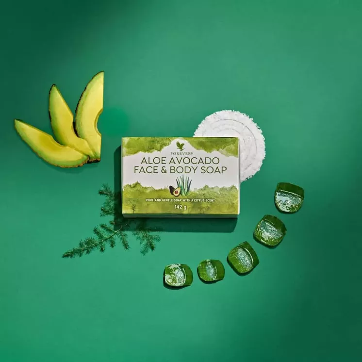 Savon Forever Aloe Avocado Soap sur un fond vert avec des tranches d’avocat et de gel d’Aloe Vera, un savon doux et hydratant.