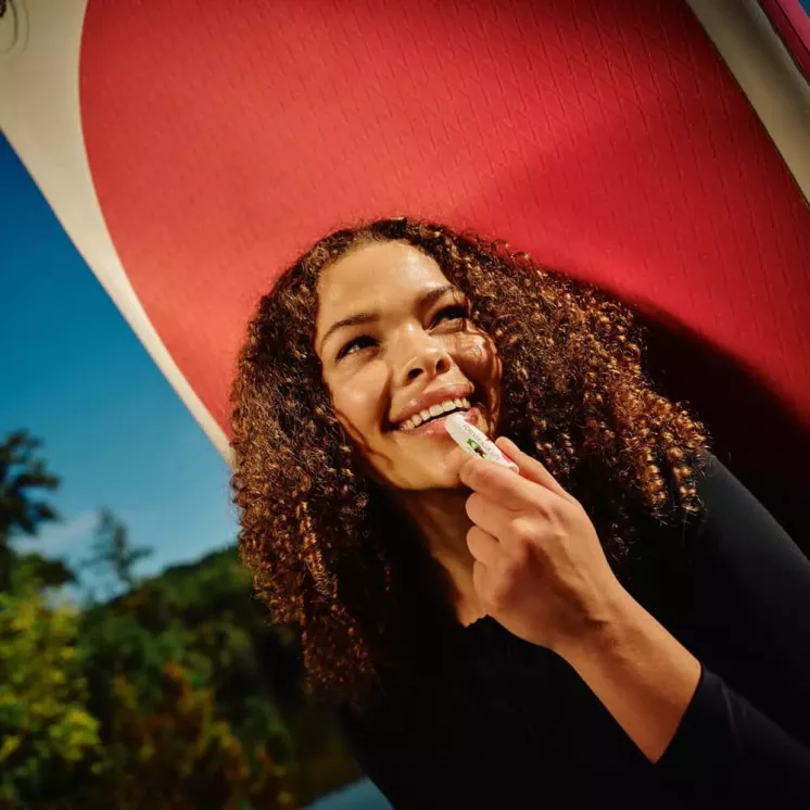 Femme souriante appliquant Forever Aloe Lips en extérieur. Baume nourrissant pour des lèvres protégées en toutes saisons.