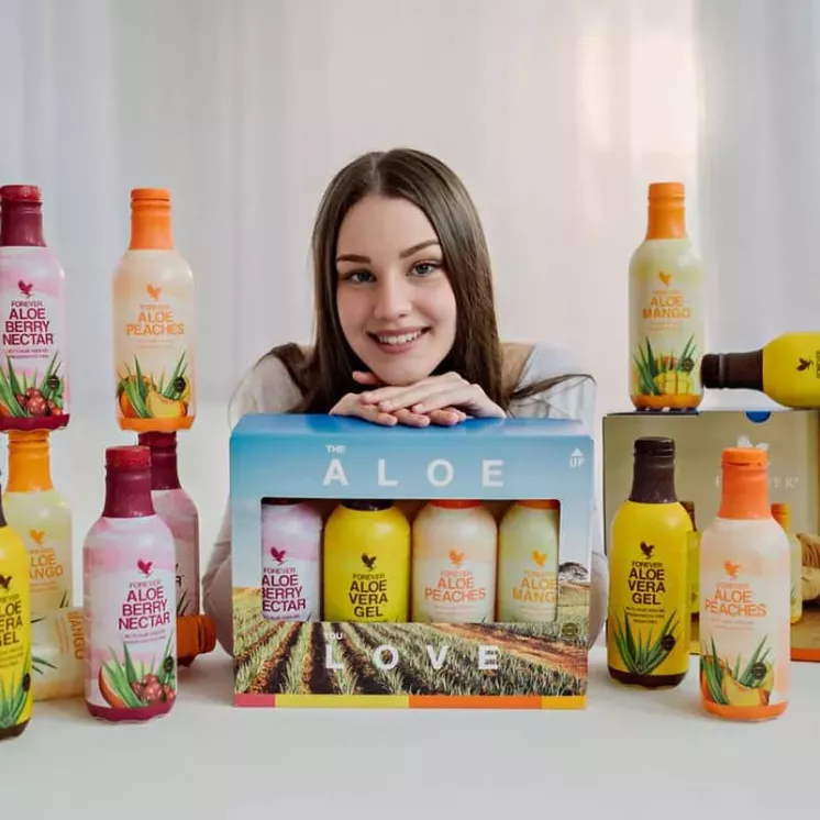 Jeune femme souriante avec un pack mix Forever Aloe Vera - 4 bouteilles visibles (nature, pêche, mangue, berry nectar)