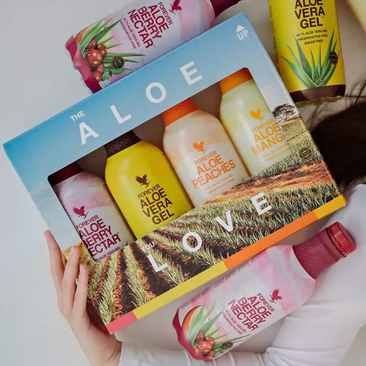 Pack mix Forever Aloe Vera dans les mains - 4 saveurs visibles avec bouteilles autour (berry nectar, mangue, pêche, nature)