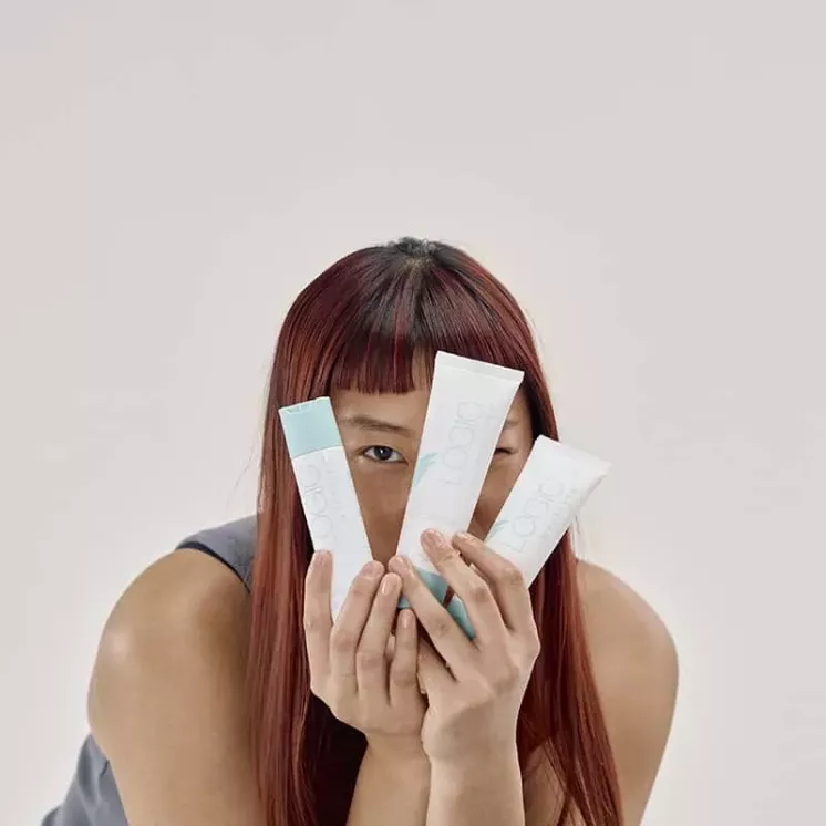 Femme tenant les trois soins visage de la Routine Logic by Forever devant son visage, sur fond neutre