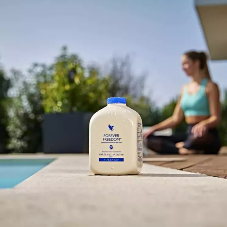 Forever Freedom en extérieur près d'une piscine, avec une femme en tenue de sport méditant en arrière-plan