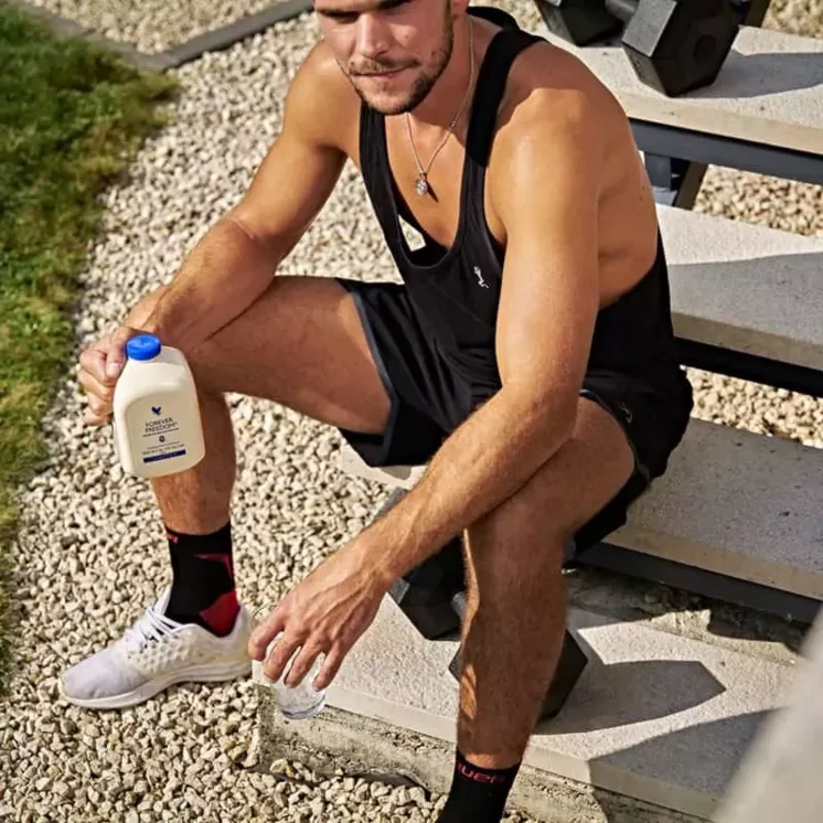 Homme sportif tenant une bouteille de Forever Freedom après l'effort, assis sur des marches en extérieur