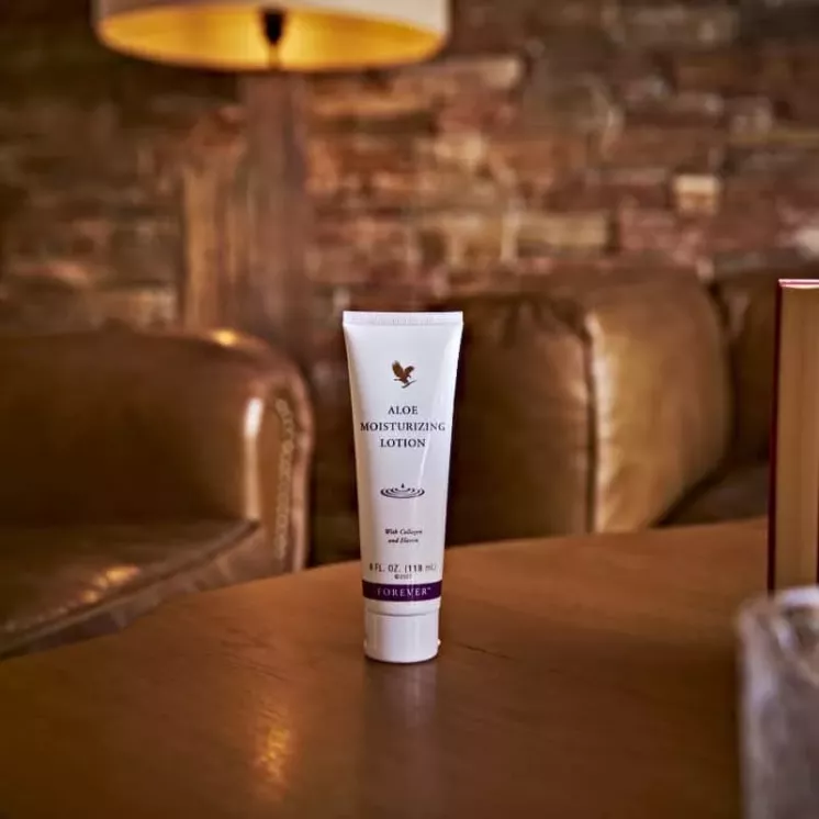 Tube de Crème Aloès Forever sur une table en bois dans un salon chaleureux avec canapé en cuir