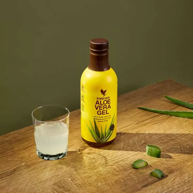 Verre de pulpe d'Aloe Vera et bouteille Forever Aloe Vera Gel sur une table en bois, avec morceaux de feuille d’aloe