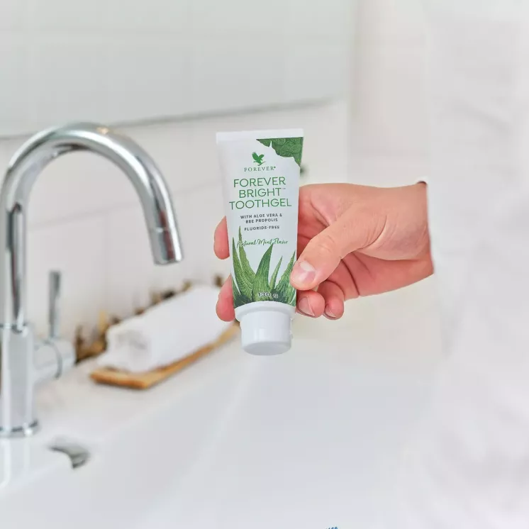 Main tenant le dentifrice Forever Bright Toothgel aloe vera dans une salle de bain moderne
