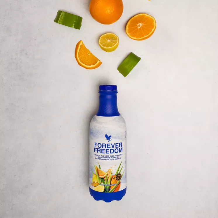 Bouteille de Forever Freedom sous des agrumes et morceaux d’aloe vera vus de dessus