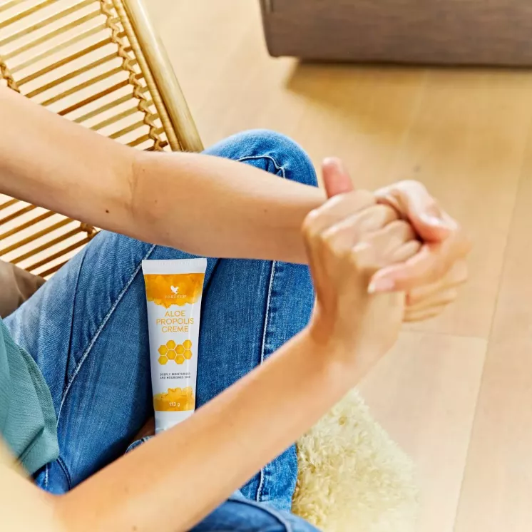 Tube Aloe Propolis Crème posé sur un jean, mains jointes en arrière-plan.