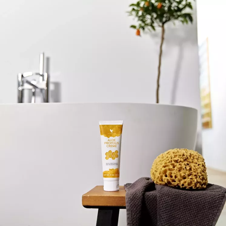 Tube Aloe Propolis Crème près d'une serviette et d'une éponge devant une baignoire.