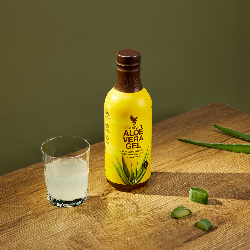 Forever Aloe Vera Gel en bouteille jaune avec verre et morceaux d'aloe vera, pour apaiser et améliorer la digestion naturellement